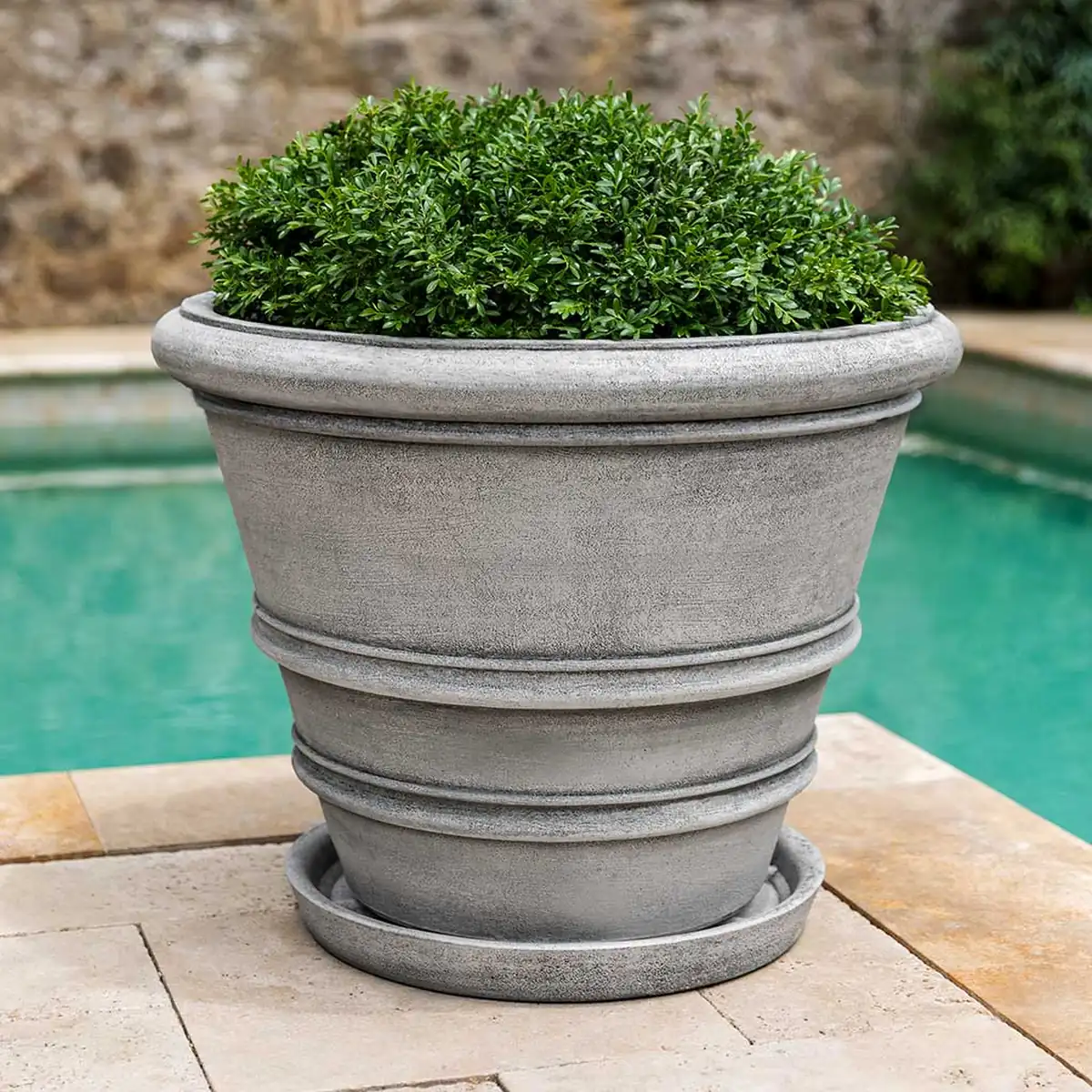 Cast stone planter saucer with large round planter on poolside patio